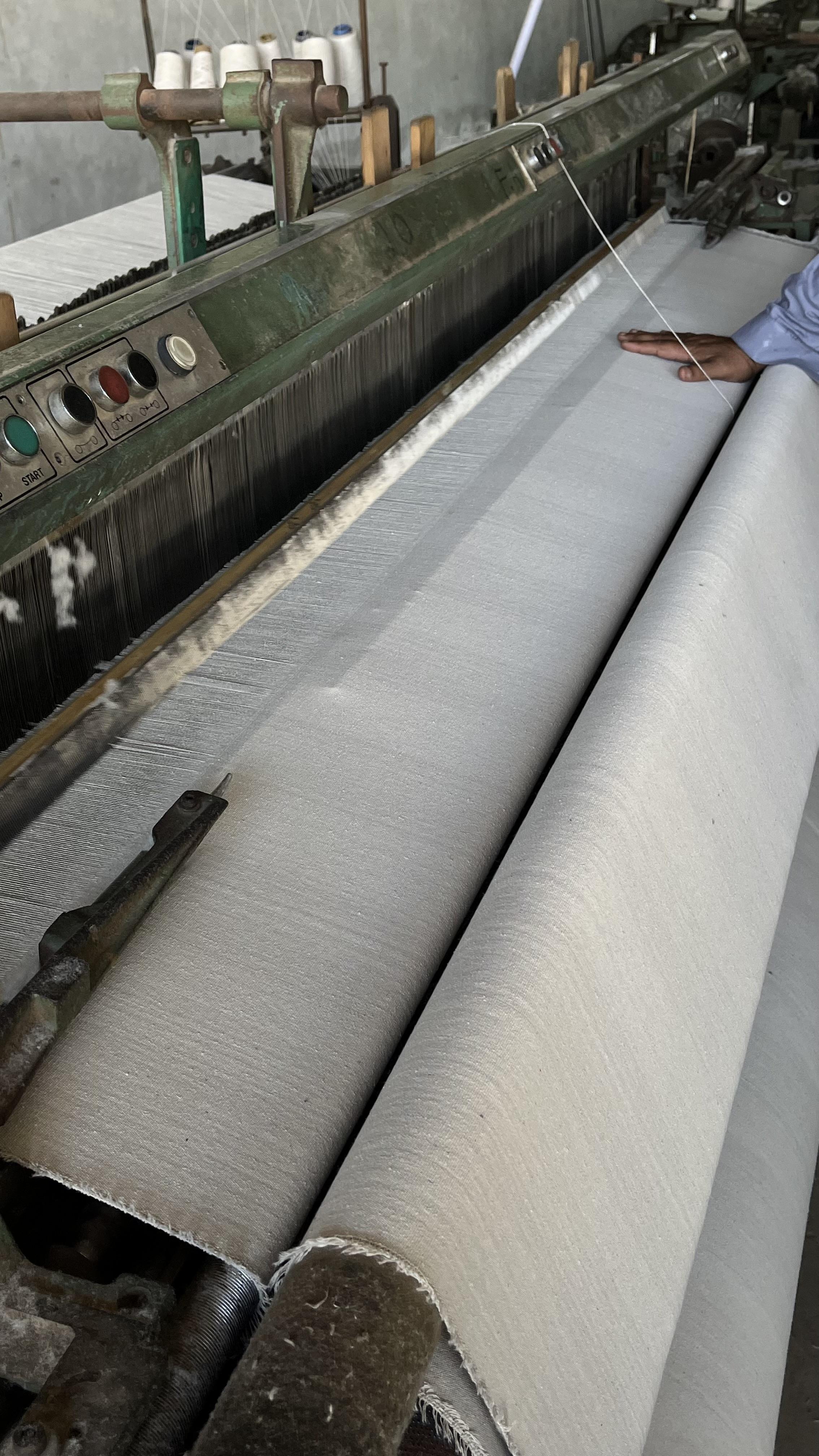 A weaver checks raw canvas coming off a loom at the Siraj Textile factory in Kasur